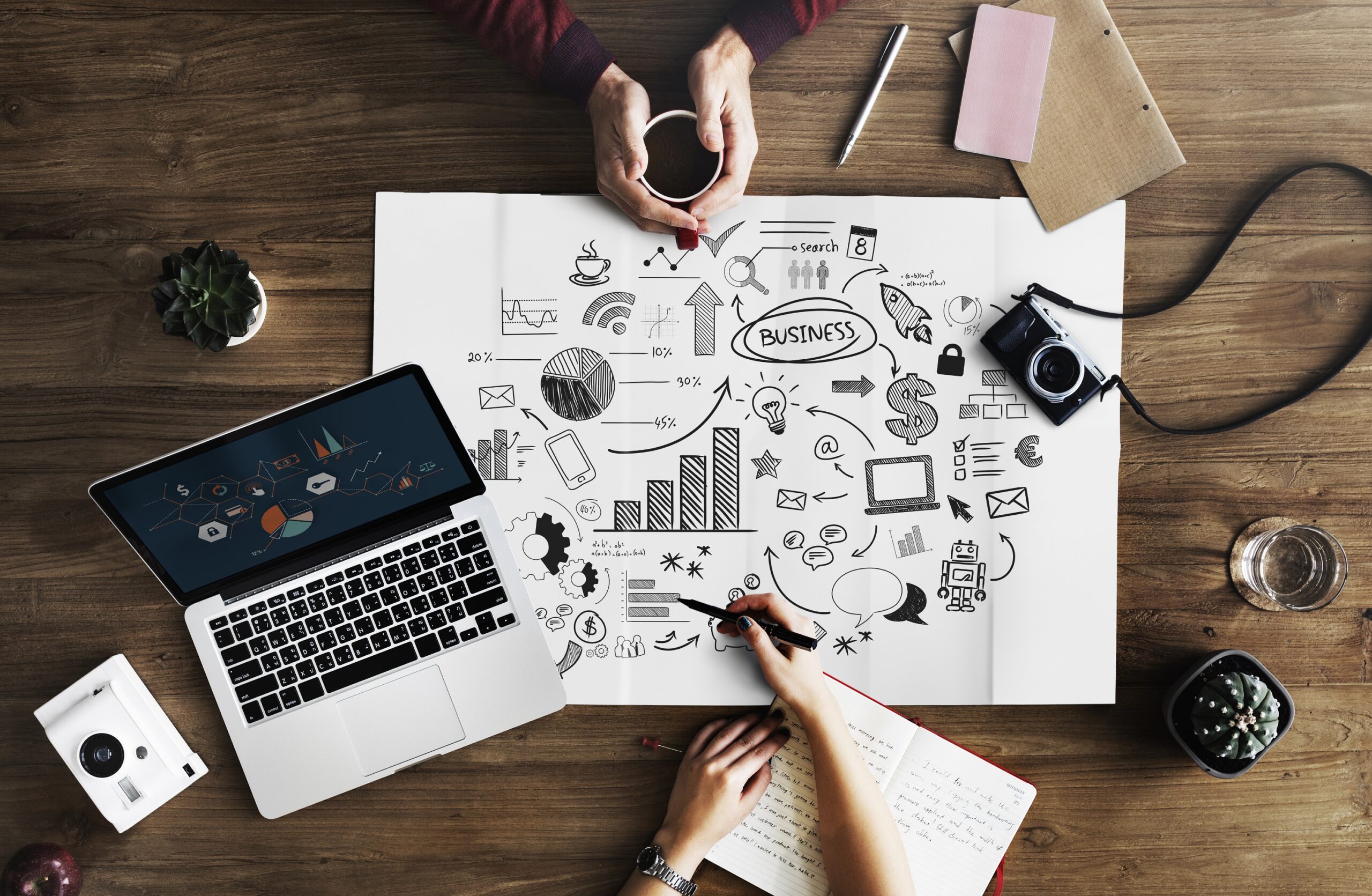 Personas planificando estrategias comerciales sobre una mesa con dibujos de datos, gráficos, tecnología y comunicación, representando claves de éxito en ventas B2B de tecnología.