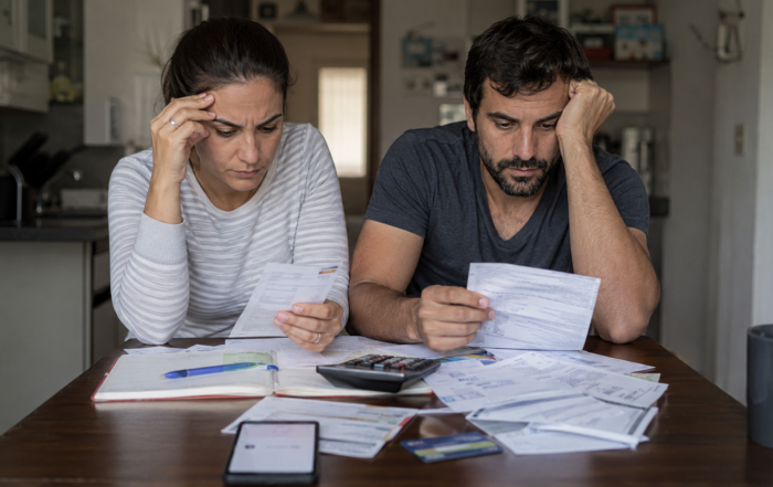 Pareja revisa facturas, resúmenes de tarjeta y papeles de crédito en una mesa del hogar, en una escena que refleja la gestión de la mora y el endeudamiento familiar en Argentina.
